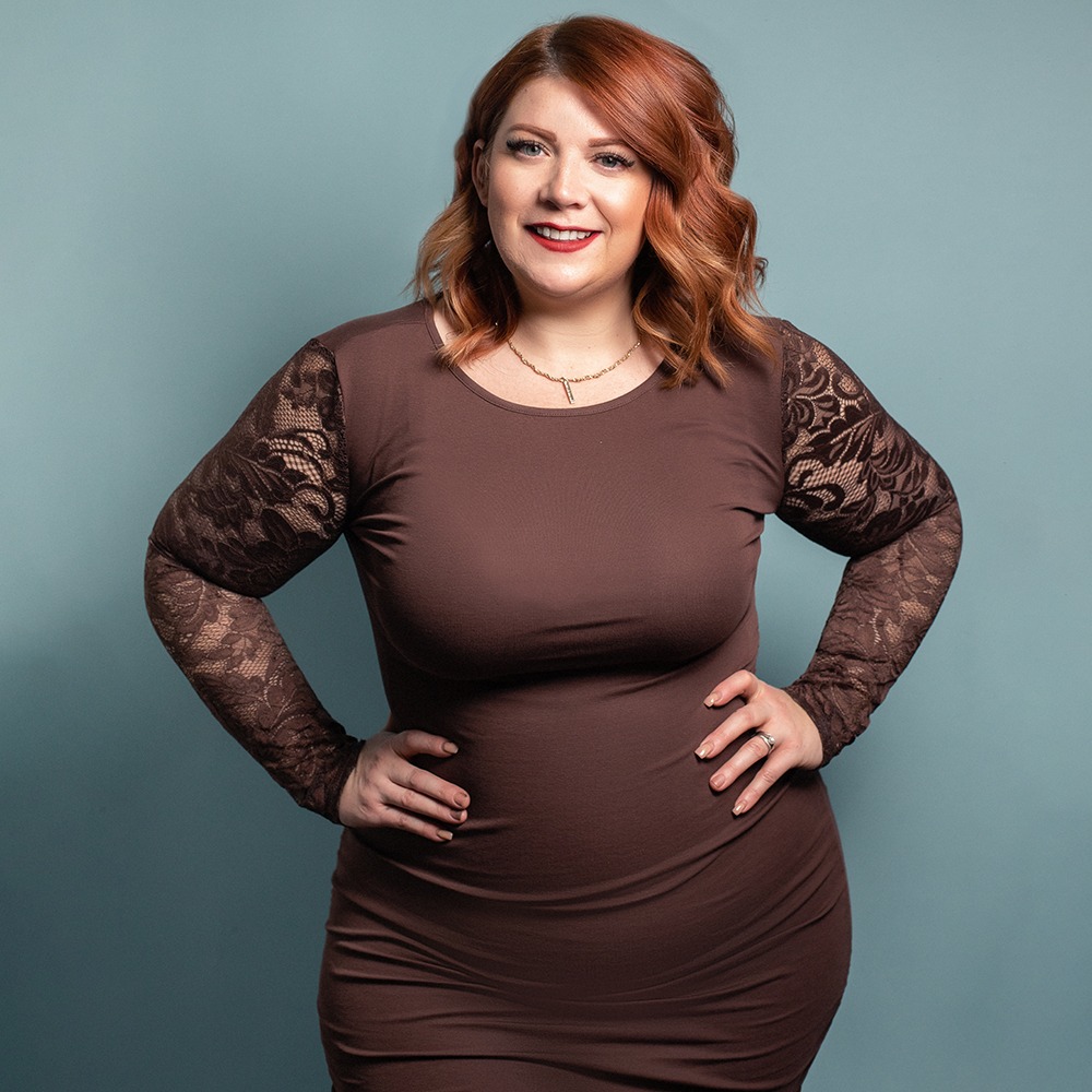 woman in brown dress with lacy sleeves smiling for portrait with her hands on her hips